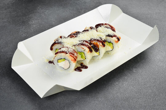 Gourmet sushi rolls topped with sweet unagi sauce and grated parmesan cheese served in white takeaway paper box. Fresh Japanese seafood meal. Delicious asian food.