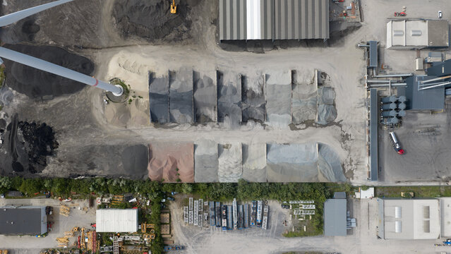 Aerial view of the industrial site at Feluy de Parc Industriel with various piles of gravel and aggregates, industrial buildings, and a wind turbine base in Seneffe, Region wallonne, Belgium.