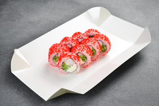 Delicious sushi rolls with tobiko caviar, cream cheese, and cucumber lie in white container. Enjoy this traditional Japanese seafood meal today. Try it.