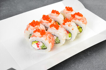 Gourmet sushi rolls topped with shrimp, mayo sauce, and red caviar in takeaway paper box. Tasty Japanese seafood with cream cheese. Fresh delicious Asian meal. © Yaruniv-Studio
