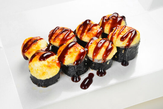 Delicious baked sushi roll set topped with creamy cheese and unagi sauce in takeaway box. Fresh Japanese rolls wrapped in nori. Tasty gourmet food.