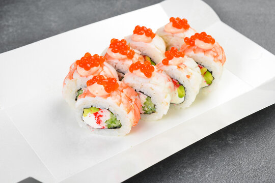 Gourmet sushi rolls topped with shrimp, mayo sauce, and red caviar in takeaway paper box. Tasty Japanese seafood with cream cheese. Fresh delicious Asian meal.