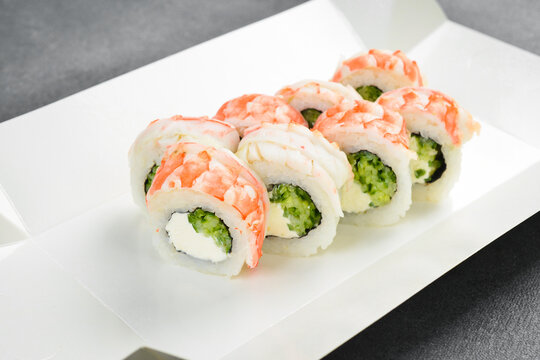 Fresh sushi rolls with tiger prawns and cream cheese are served in a white paper tray. Enjoy this tasty Japanese appetizer on grey background. Order now.