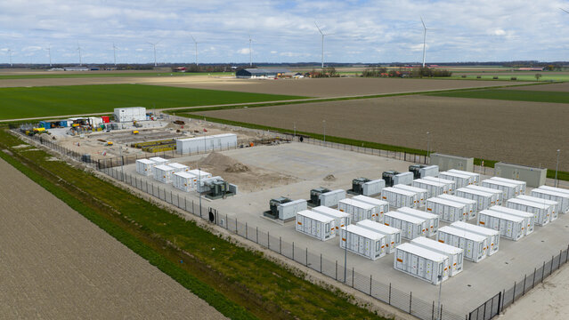 Aerial view of a battery energy storage system facility with rows of white containers and electrical equipment in a rural landscape with wind turbines in Dronten, Flevoland, Netherlands.