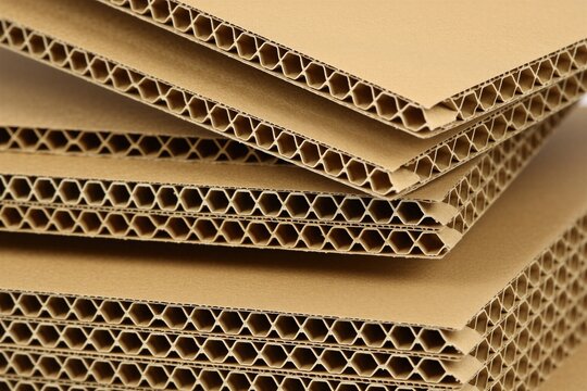Stack of corrugated cardboard sheets, light brown color with hexagonal interior structure. Material for packaging and protection during transport. Recyclable and eco friendly paper product.