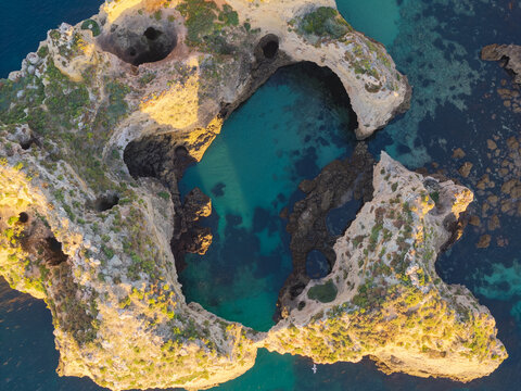 Aerial view of the dramatic limestone cliffs and sea caves of Ponta da Piedade with turquoise water and golden sunlight in Lagos, Faro District, Portugal.