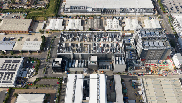Aerial view of a large industrial data center complex with cooling units on the roof, surrounded by warehouses and parking areas in Slough, England, United Kingdom.