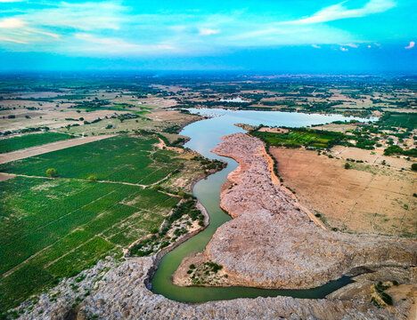 Aerial view of a winding river flowing through lush green agricultural fields and arid landscape in Dera Ghazi Khan, Punjab, Pakistan.