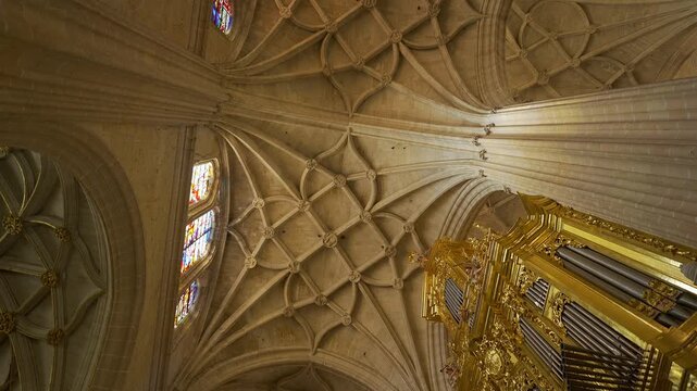 Upward view of ribbed Gothic vaults stained glass windows and golden organ pipes