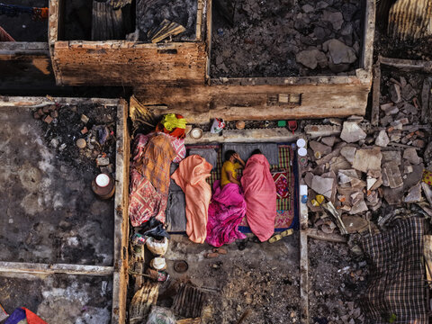 Aerial view of people sleeping on mats under colorful blankets amidst the debris of a burnt structure in Korail Basti, Dhaka, Dhaka Division, Bangladesh.
