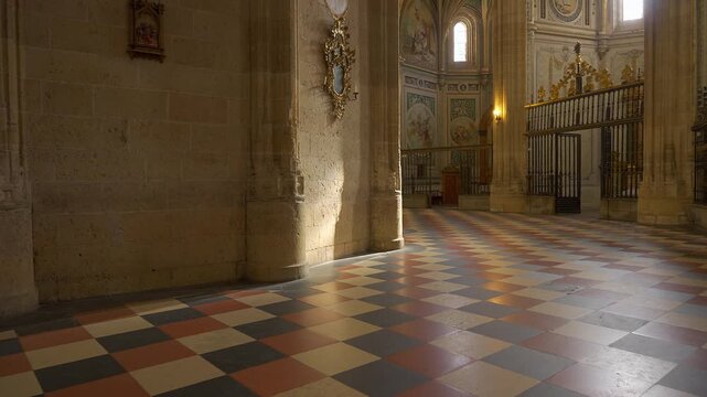 Sunlight crossing the patterned cathedral floor beside stone columns and chapel gates