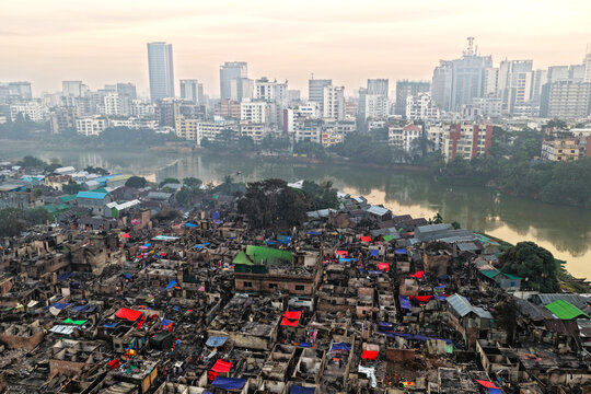 Aerial view of the aftermath of a fire in the Korail Basti slum, showing charred structures and debris near the lake with the Dhaka skyline, Dhaka, Dhaka Division, Bangladesh.