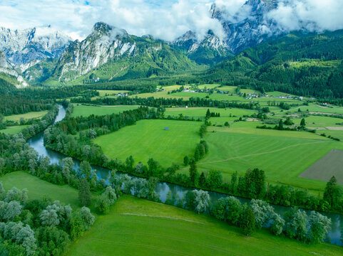 Aerial view of Nationalpark Gesause with the Enns river winding through lush green meadows and dense forests under dramatic mountain peaks in Admont, Steiermark, Austria.