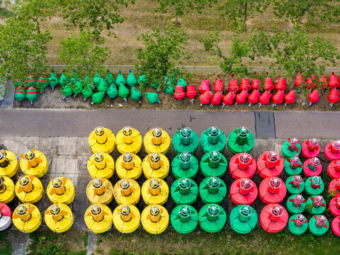 Aerial view of Rijkswaterstaat Harderhaven featuring rows of colorful yellow, green, and red navigation buoys stored on a paved surface in Zeewolde, Flevoland, Netherlands.
