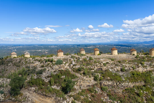 Aerial view of Moinhos da Serra da Atalhada, a series of historic stone windmills situated on a rocky ridge under a clear blue sky in Penacova, Coimbra, Portugal.