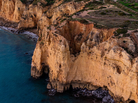 Aerial view of Ponta da Piedade featuring dramatic golden limestone cliffs, sea caves, and turquoise Atlantic waters along the coastline in Lagos, Faro, Portugal.