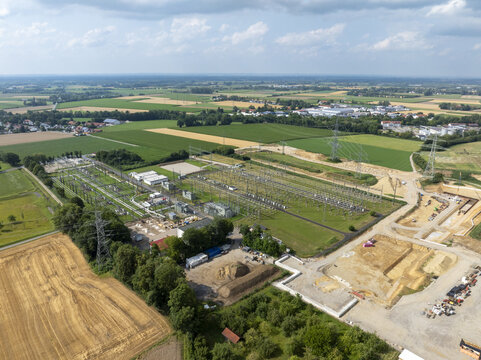 Aerial view of Neufinsing electrical substation with transformers, power lines, and switchyard equipment surrounded by agricultural fields and construction areas in Finsing, Bayern, Germany.