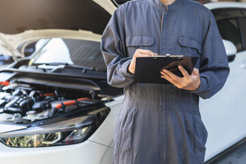 Fototapeta premium Auto check up and car service shop concept. Mechanic writing job checklist to clipboard to estimate repair quotation to client at workshop garage.