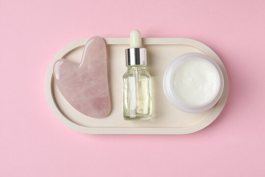 Cosmetic cream, beauty serum oil bottle and quartz face gua sha on pink background. Natural skin care