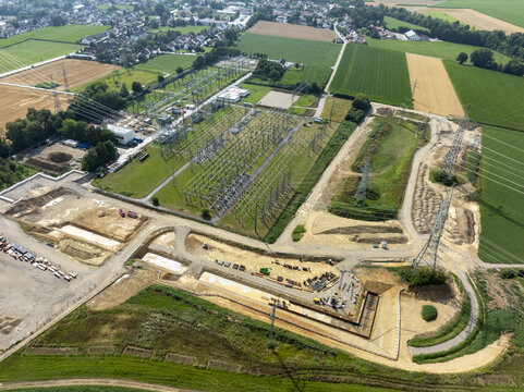 Aerial view of the Neufinsing electrical substation with power lines, construction equipment, and surrounding agricultural fields in Finsing, Bayern, Germany.