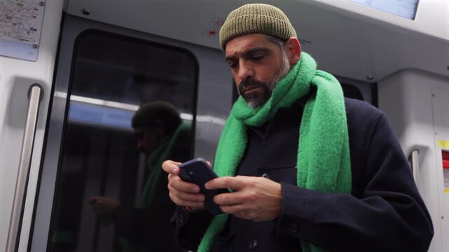 Mature bearded man using his smartphone for messaging, typing, and browsing social media while commuting on a subway train during his journey through the city