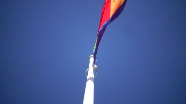 Stockholm, Sweden A Pride flag flies on a flagpole against a blue sky. 