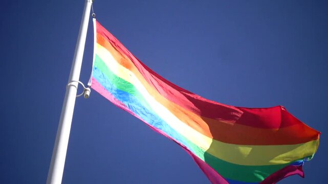 Stockholm, Sweden A Pride flag flies on a flagpole against a blue sky. 