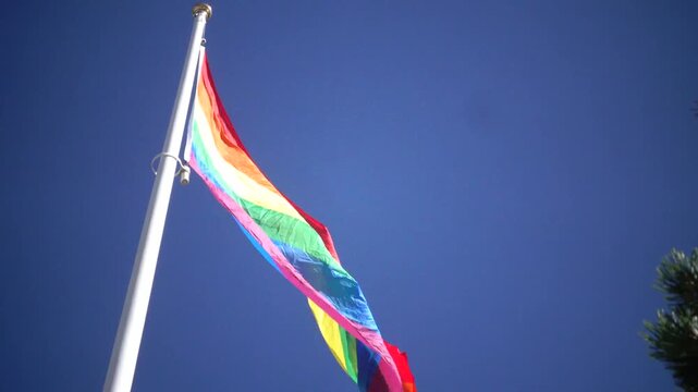 Stockholm, Sweden A Pride flag flies on a flagpole against a blue sky. 