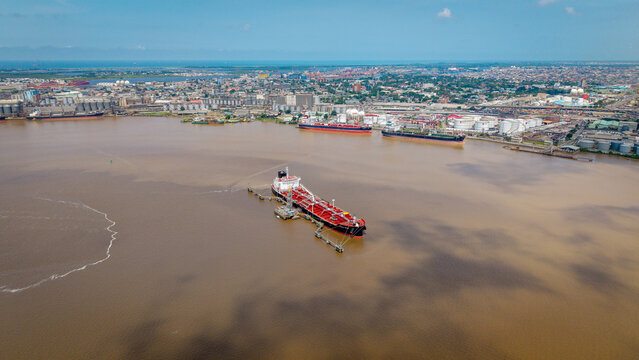 Aerial view of a large oil tanker docked at a terminal in the harbor with industrial port facilities and the city skyline in the background in Lagos, Lagos, Nigeria.