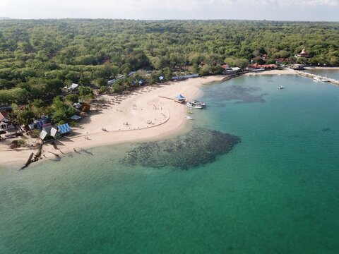 Aerial view of a sandy beach with turquoise water, coral reefs, small boats, and lush greenery along the coastline in Sumenep, East Java, Indonesia.