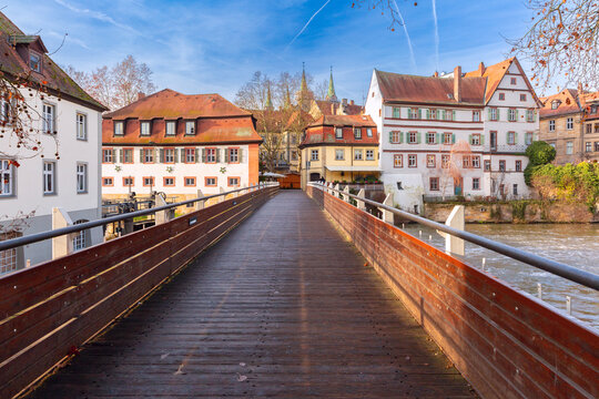 Wooden pedestrian bridge crossing the Regnitz River with traditional buildings in the historic center of Bamberg, Bavaria, Germany.
