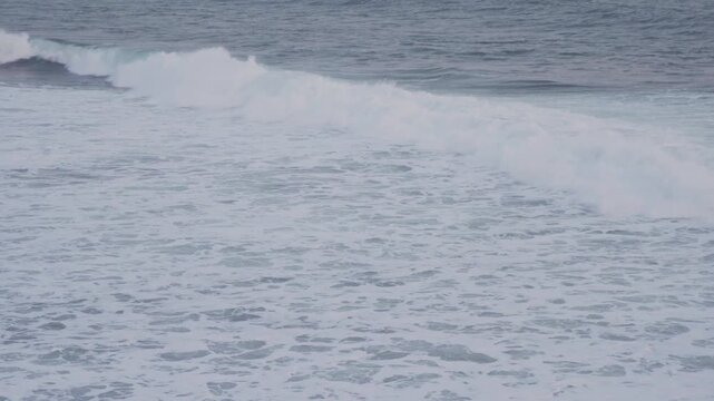 Large waves rolled in the middle of the sea, with white foam visible. Elevated view