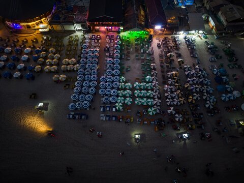 Aerial view of a beach at night featuring rows of illuminated beach umbrellas and lounge chairs arranged along the sandy shoreline in Ghana.