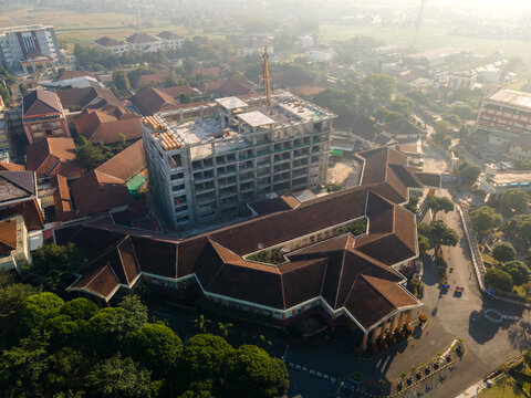 Aerial view of a large administrative complex featuring a building under construction, surrounded by brown-tiled roof buildings, trees, and roads in Banyumas Regency, Central Java, Indonesia.