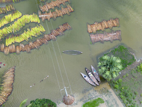 Aerial view of Patul with jute plants soaking in water for the retting process alongside traditional wooden boats and a power line pole in Natore District, Rajshahi Division, Bangladesh.