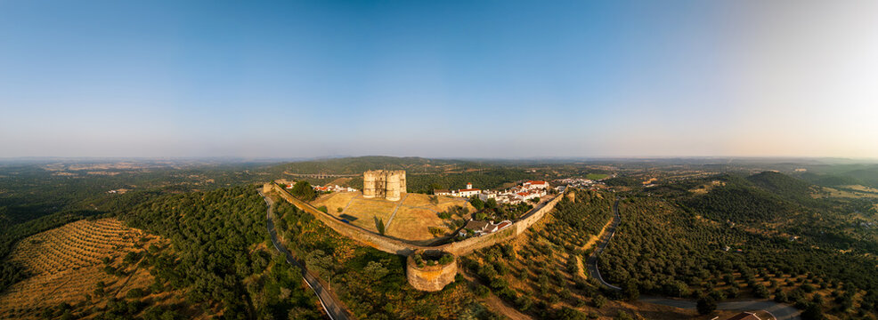 Aerial view of Castle of Evoramonte surrounded by historic stone walls, olive groves, and rolling hills under a clear blue sky in Evora Monte, Distrito de Evora, Portugal.