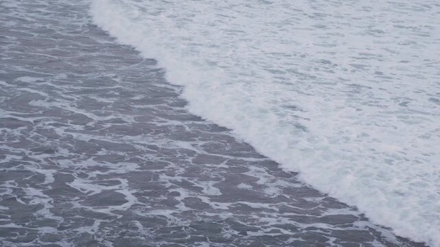 Large waves rolled in the middle of the sea, with white foam visible. Elevated view