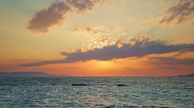 Stunning golden sunset paints sky vibrant hues over calm ocean. Gentle waves lap the shore, with distant mountains creating serene picturesque backdrop. Evokes tranquility natural beauty.