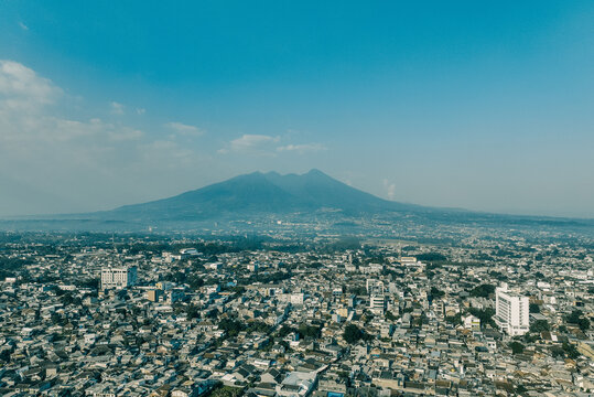 Aerial view of the dense urban landscape of Bogor Timur with Mount Salak in the background, featuring residential rooftops and commercial buildings in Bogor Timur, West Java, Indonesia.