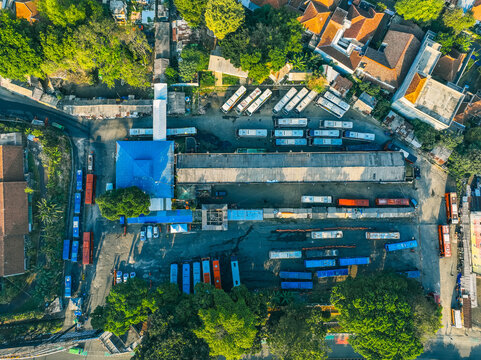 Aerial view of Baranangsiang bus terminal with rows of parked buses, surrounding lush trees, and urban infrastructure in Bogor Timur, West Java, Indonesia.
