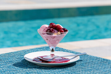 Obraz premium Berry ice cream with cherries and raspberries served in glass dessert bowl by swimming pool on sunny summer day