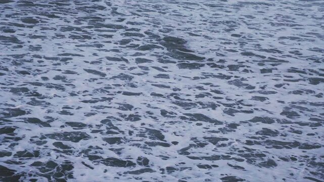 Large waves rolled in the middle of the sea, with white foam visible. Elevated view