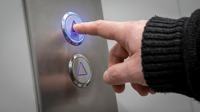 Finger pressing illuminated up arrow button on modern stainless steel elevator control panel with elevator stainless technology building navigation