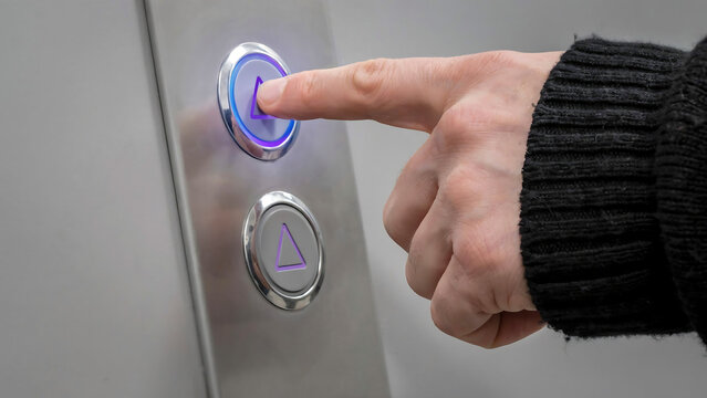 Close-up of human finger pressing a modern illuminated elevator button with elevator technology building indicator navigation interior