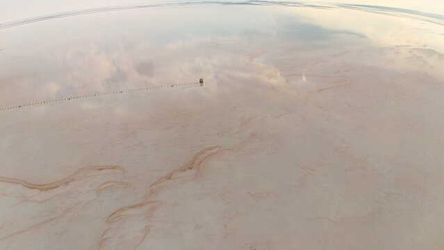 Aerial view of the vast, reflective surface of the Koyuncu Salt Works at Lake Tuz, with calm water mirroring the sky and subtle patterns in the salt crust in Sereflikochisar, Ankara, Turkey.