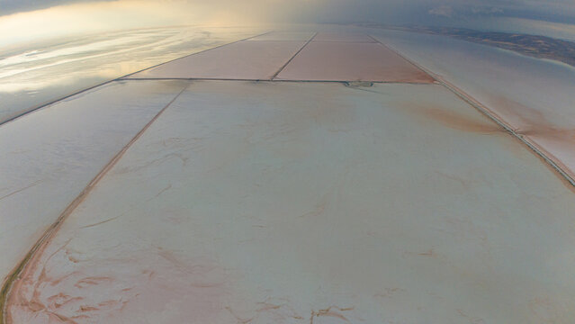 Aerial view of the Koyuncu Salt Works, featuring expansive salt pans with pinkish hues and geometric divisions under a soft sky in Sereflikochisar, Ankara, Turkey.