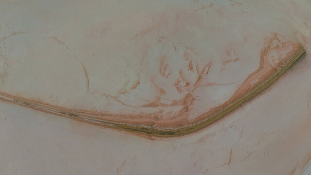 Aerial view of the Koyuncu Tuz Isletmesi salt lake with its distinctive pinkish salt crust and a narrow causeway cutting through the landscape in Sereflikochisar, Ankara, Turkiye.