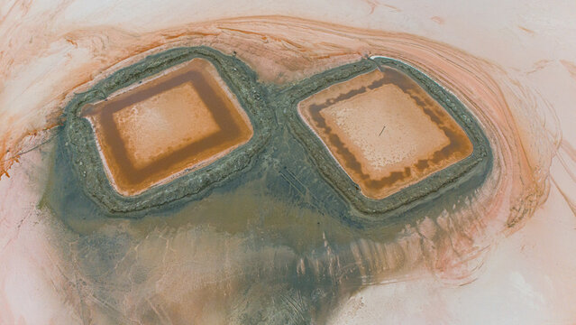 Aerial view of the Koyuncu Salt Works featuring two square evaporation ponds with vibrant pinkish-orange water surrounded by textured earth in Sereflikochisar, Ankara, Turkey.