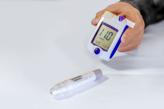 Man holding a blood glucose meter showing a high blood sugar level with a lancet pen on the table
