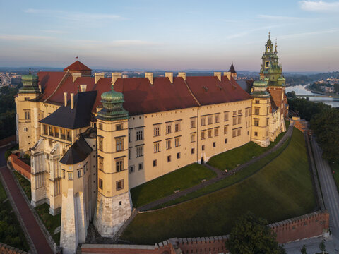 Aerial view of Wawel Royal Castle illuminated by golden hour light with historic architecture and green slopes in Krakow, Malopolska, Poland.